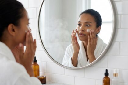 Femme appliquant une crème hydratante visage devant un miroir de salle de bain, routine de soin de la peau avant l'été