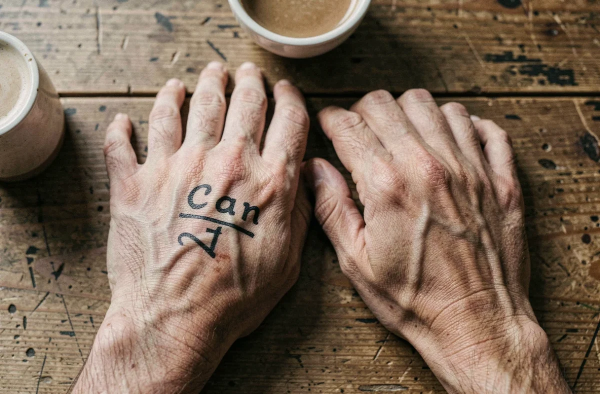 Tatouage prénom en lettres capitales sur les doigts d'une main posée sur une table en bois, encre cicatrisée